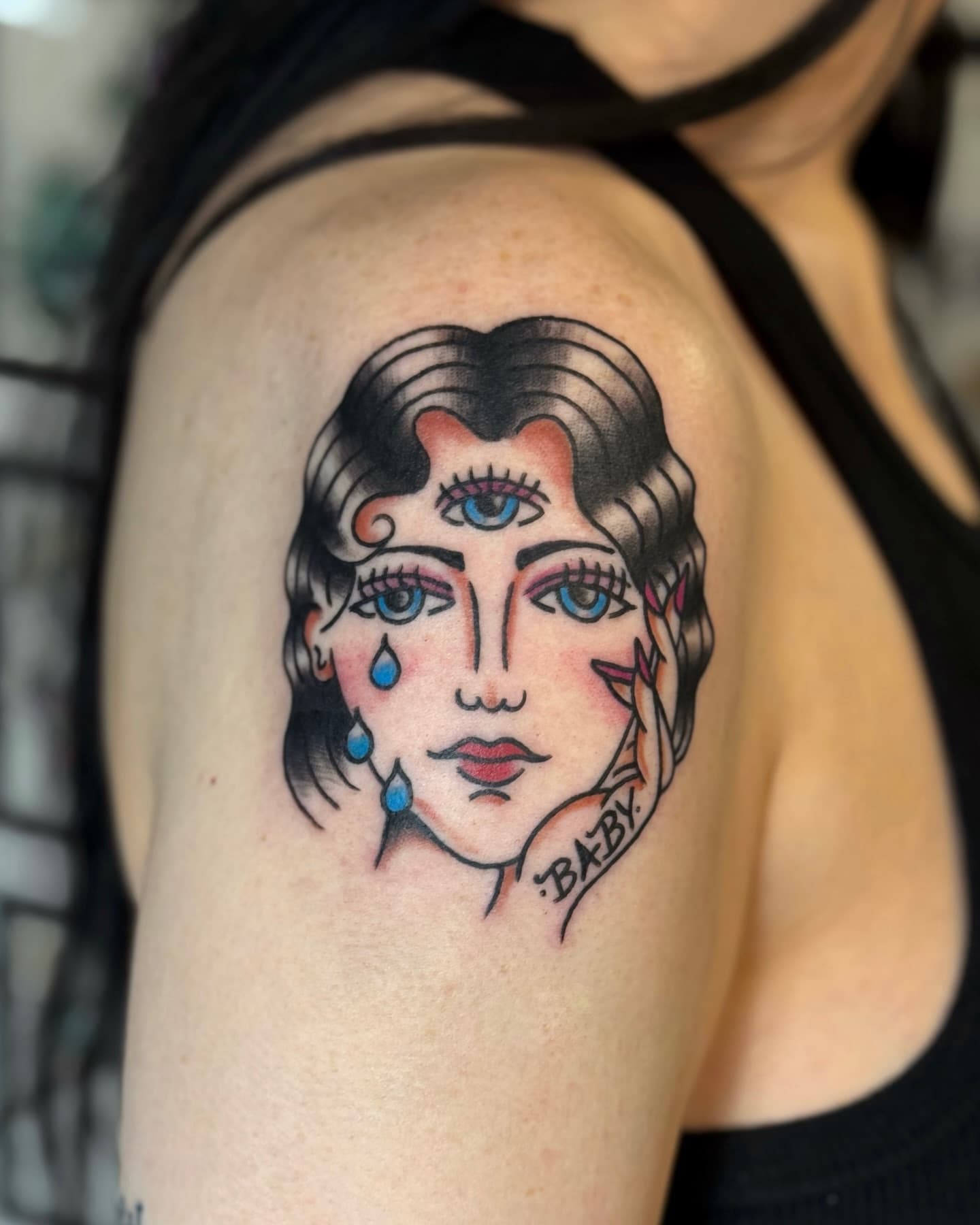 Traditional tattoo of a woman with three eyes crying. Her hand is caressing her face with a baby tattoo on the side