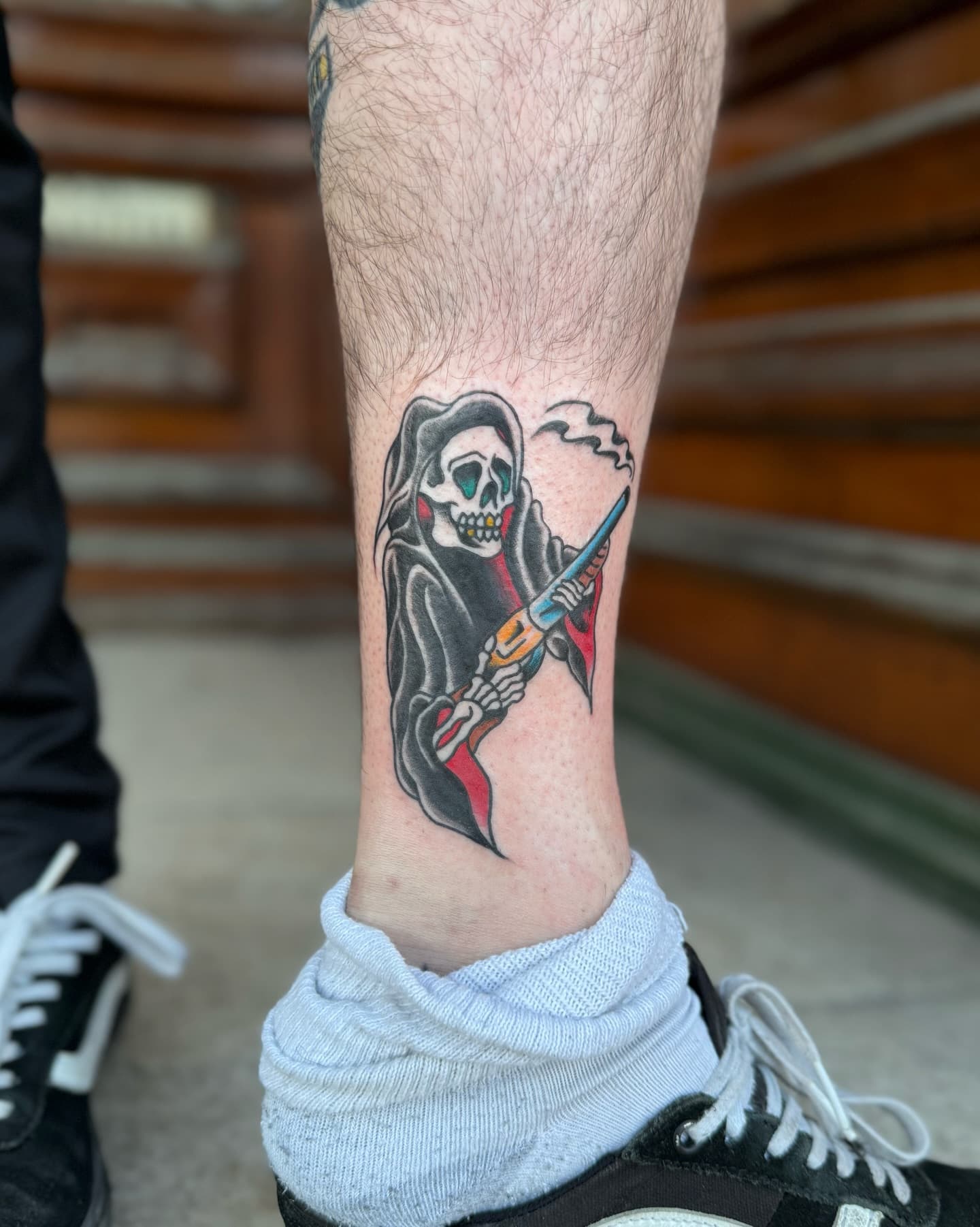 Traditional style tattoo of a grim reaper holding a smoking shot gun.