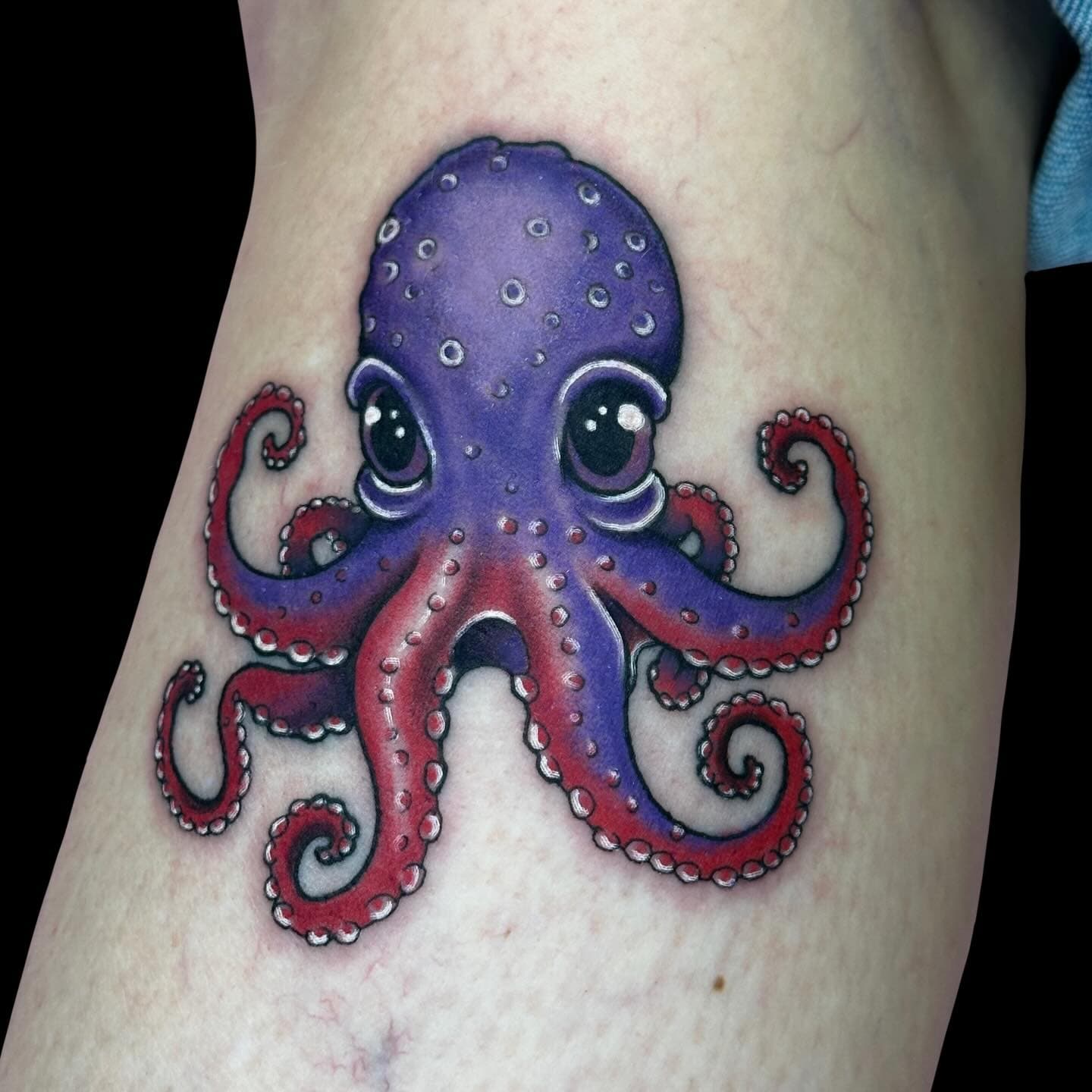 Tattoo of a purple octopus with wide eyes.