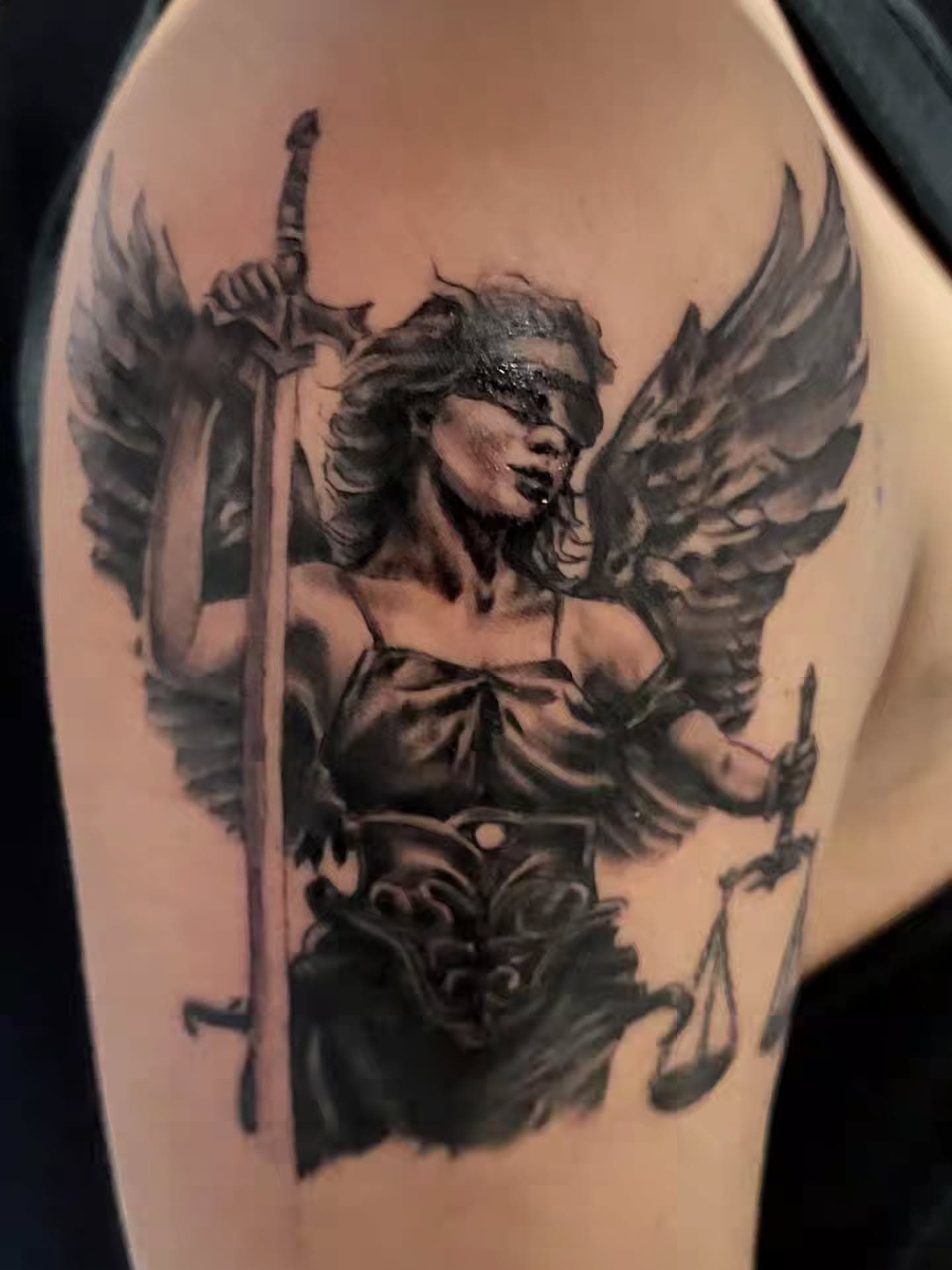 Angel tattoo with a sword in one hand and a balance scale in the other
